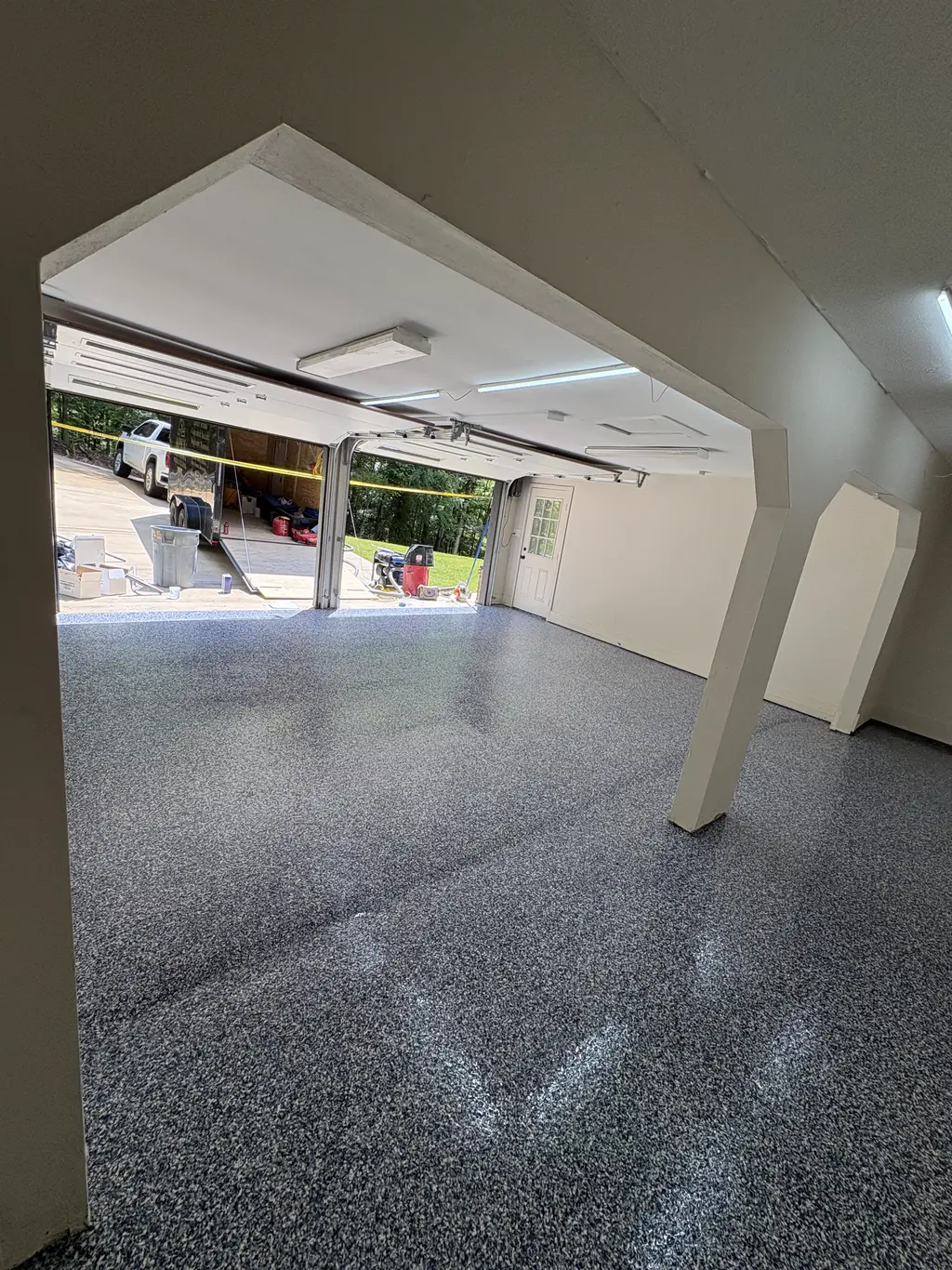 Open garage bay with support columns and a gray flake epoxy floor