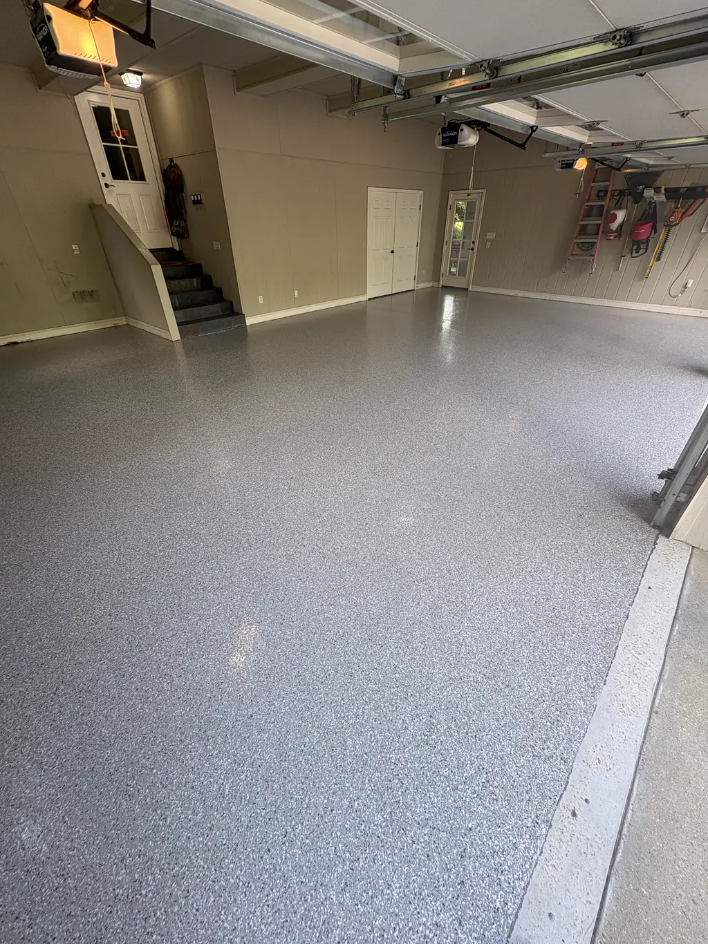 Residential garage interior with a light flake epoxy floor and stairs to the house