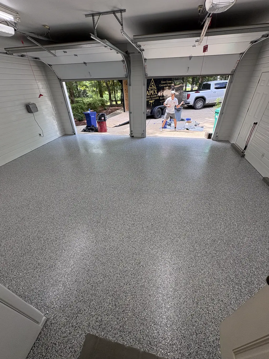 Two car garage with a light gray flake epoxy floor and the door open to a driveway
